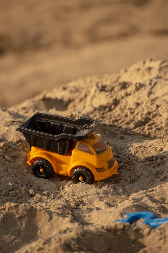 Close-up of a yellow toy dump truck on sand, emphasizing playtime outdoors.