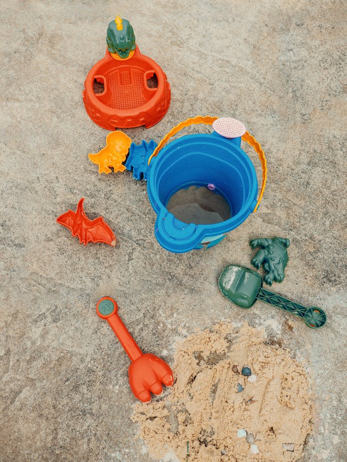 Bright plastic beach toys scattered on sand, perfect for summer fun.