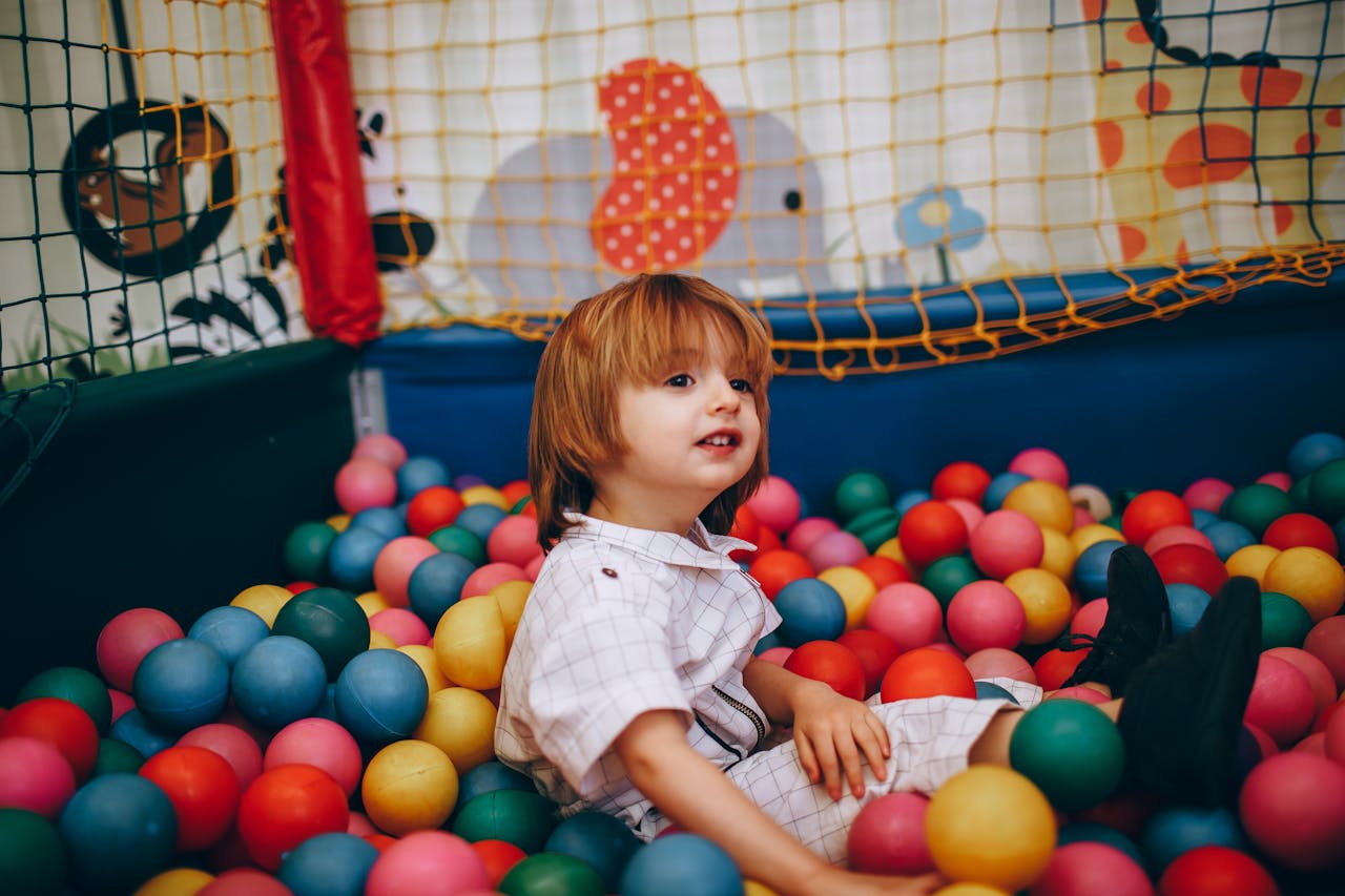 A child sits happily in a vibrant ball pit at an indoor play area.