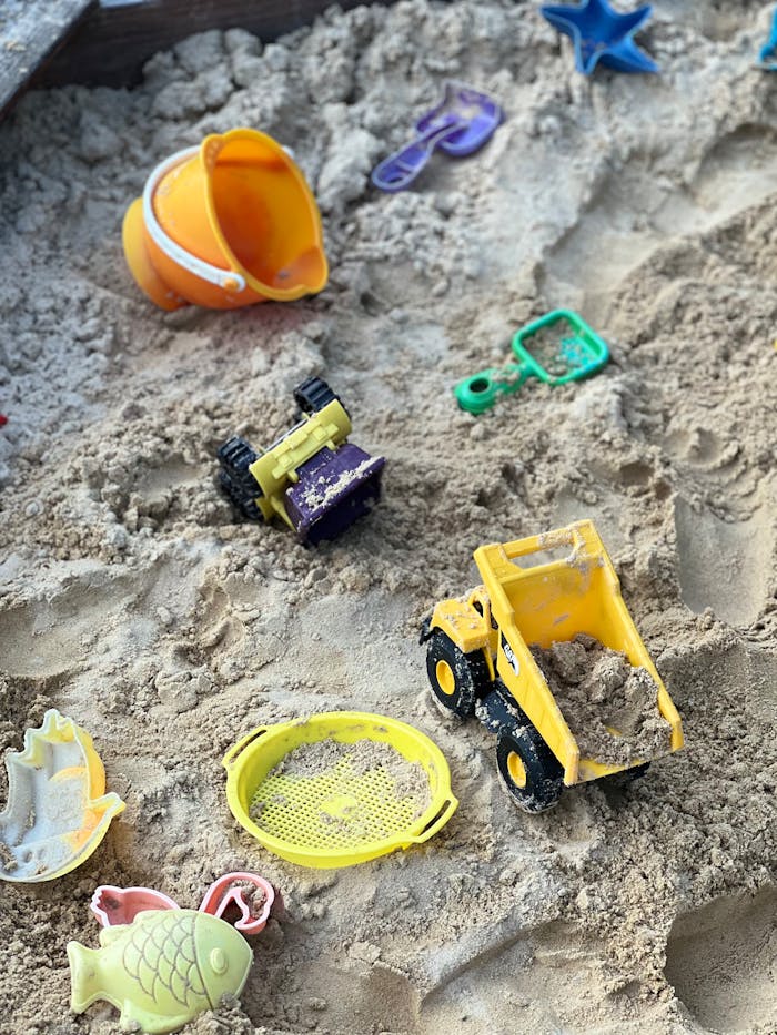 Vibrant plastic toys scattered in a sandy playground sandbox.