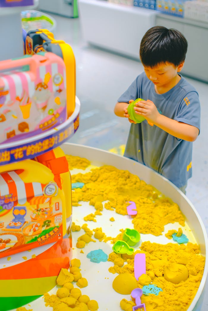 A young boy enjoys playing with colorful kinetic sand and toys indoors.