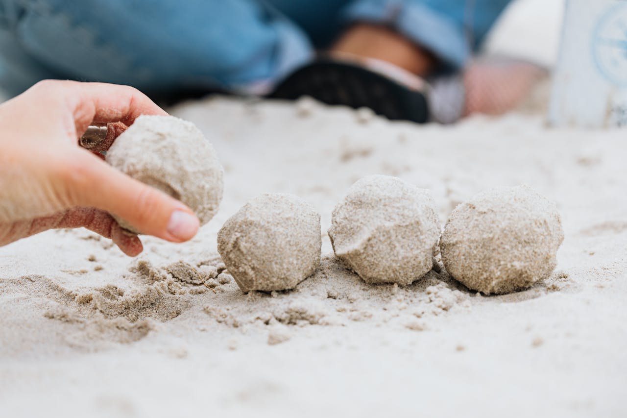 A hand forming round sand balls on a beach, close-up view.