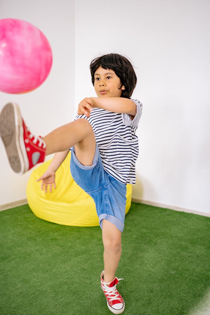 Child enjoying active play indoors, kicking a vibrant pink balloon with enthusiasm.